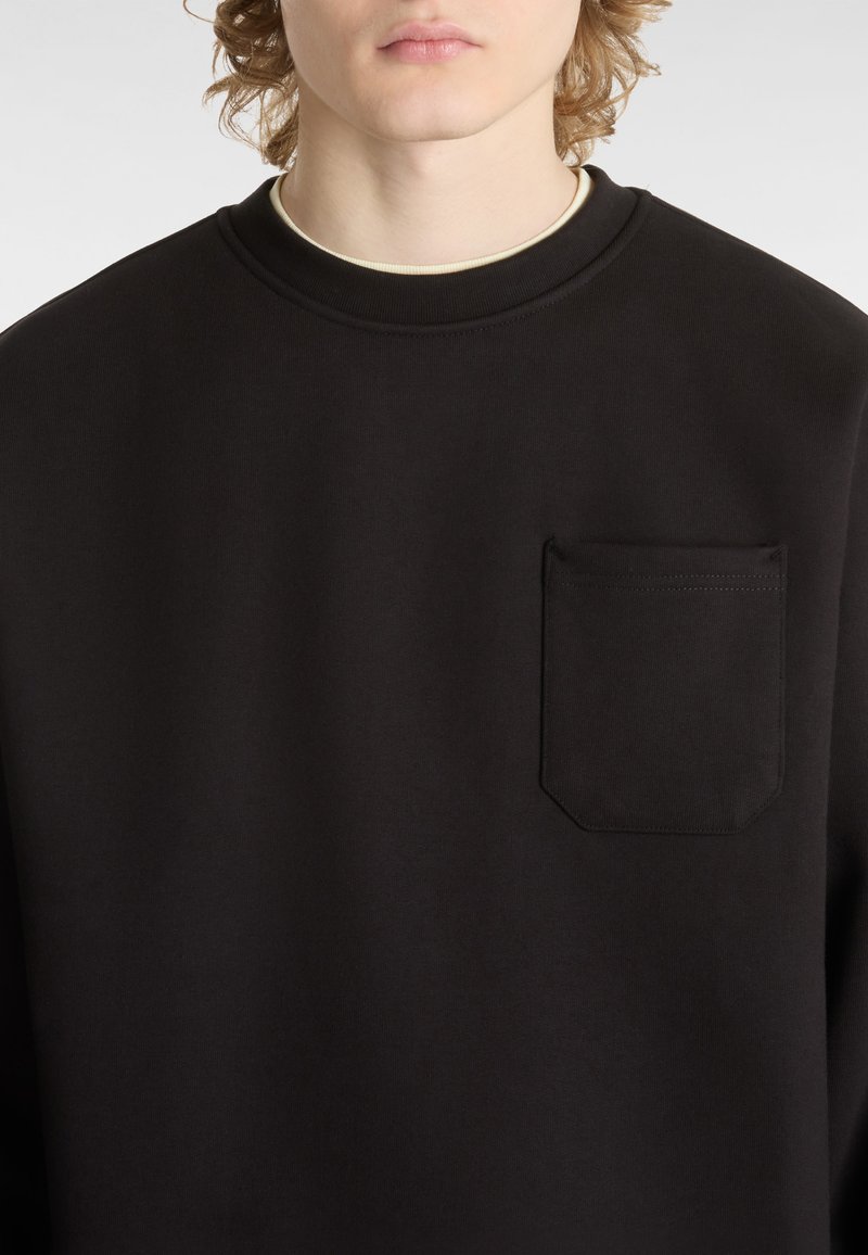 Zwarte sweatshirt met een ronde hals, een structuurstof en een klein borstzakje met afgeronde randen.