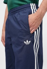 Ναυτικό μπλε αθλητικό παντελόνι με λευκές ρίγες και κεντημένο λογότυπο. Διαθέτει τσέπη με φερμουάρ και ελαστική μέση για ρυθμιζόμενη εφαρμογή.