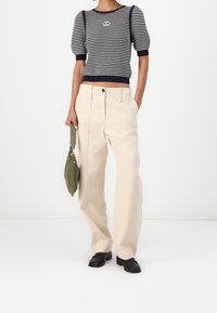 Pruhovaný námořnický a bílý zkrácený pletený svetr, béžové široké kalhoty, zelená kabelka a černé boty. Výrazné pro nabírané rukávy a zapínání na knoflíky.