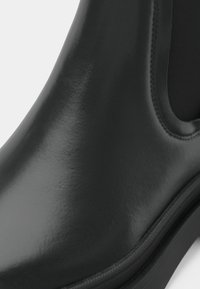 Detailný záber na hladkú čiernu koženú čižmu s elastickým bočným panelom a viditeľným švom pozdĺž podrážky a horného okraja.