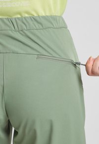 Pantaloni sportivi verdi con fascia elastica in vita e tasca con cerniera sul retro. Tessuto liscio e leggero, adatto per l'abbigliamento attivo.