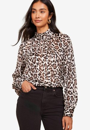 Langärmlige Bluse im Leopardenmuster mit hohem Hals und Falten, aus leichtem Stoff, kombiniert mit schwarzen Jeans.