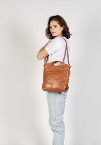 Bruine leren tote bag met een gladde, gestructureerde afwerking, voorzien van een open bovenkant en een verstelbare schouderband.