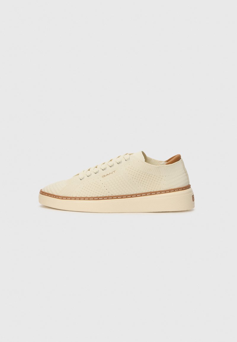 Sneakers beige con una parte superiore in maglia testurizzata, punta rotonda, suola piatta e cuciture marroni a contrasto. Presentano un piccolo logo sul lato.