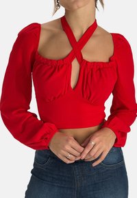 Blouse rouge courte avec manches bouffantes et décolleté plongeant. Présente des accents froncés et un design de bretelles croisées. Texture lisse.