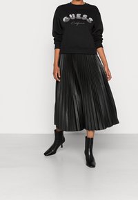 Černá mikina se stříbrným potiskem "GUESS California". Kombinována s černou plisovanou midi sukní z umělé kůže a boty na podpatku.