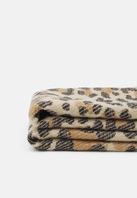 Couverture en laine beige pliée avec un motif léopard noir et marron sur fond blanc.