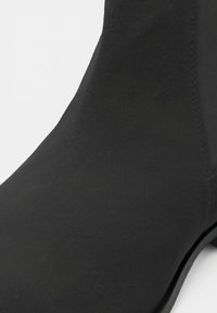 Gros plan d'une bottine en cuir noir montrant une texture lisse et un détail de couture sur le côté.