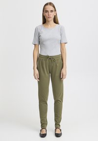 Grijs geribd T-shirt met korte mouwen gecombineerd met groene broek met trekkoord. De broek heeft een losse pasvorm en is gemaakt van zachte, lichte stof.