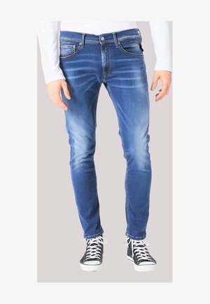 Slim-fit blue denim jeans with faded wash worn by a person in black and white sneakers and a white long-sleeve top.