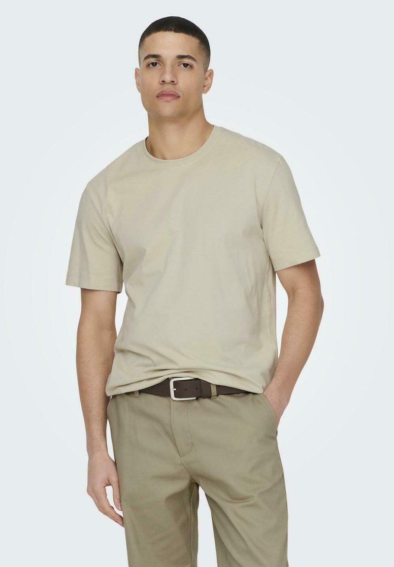Beige Baumwoll-T-Shirt mit kurzen Ärmeln und Rundhalsausschnitt, kombiniert mit olivgrünen Hosen und einem braunen Gürtel, im schlichten Design.