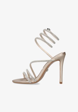 Sandaal met hoge hak en metallic afwerking, met drie bandjes van strass over de voet en een spiraalvormige enkelband van strass op een witte achtergrond.