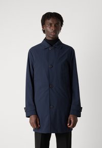 Tums zila iegarena mēteli ar norādītu apkakli, priekšējo pogu, sānu kabatām un pogātām aprocēm, kas izgatavots no gluda, ūdensizturīga auduma.