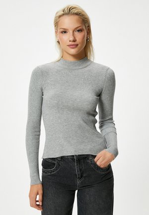 Maglione a maniche lunghe a coste grigio chiaro con collo alto, dalla silhouette attillata e con spacchi laterali, abbinato a jeans in denim scuro con cuciture evidenti.
