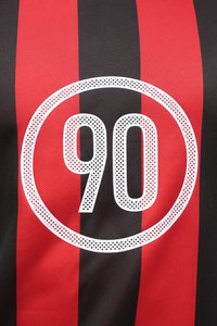 Μαύρη και κόκκινη ριγέ μπλούζα με μεγάλη λευκή κυκλική γραφική παράσταση με το "90" στο κέντρο, κατασκευασμένη από αναπνεύσιμο ύφασμα.