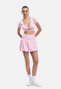 Top corto rosa con detalle de frente retorcido y mangas cortas, combinado con una mini falda acampanada a juego, ambas hechas de una tela suave.