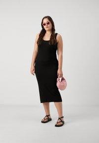 Svart ribbet tankkjole med mellomlang lengde, sammen med svarte sandaler med stropper og en liten rosa håndveske. Modell med rosa solbriller.