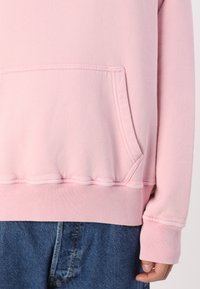 Un sweatshirt rose avec une poche kangourou, des poignets et un ourlet côtelés. Texture douce avec une coupe décontractée, associé à un jean en denim noir.