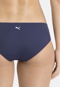Bikini-Hose in Marineblau aus glattem Material. Mit dem charakteristischen weißen Puma-Logo auf der Rückseite, niedrig geschnitten und minimalistisch im Design.