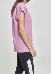 Camiseta de algodón rosa con mangas enrolladas y un corte relajado, combinada con leggings negros que presentan paneles laterales blancos. Diseño simple y casual.