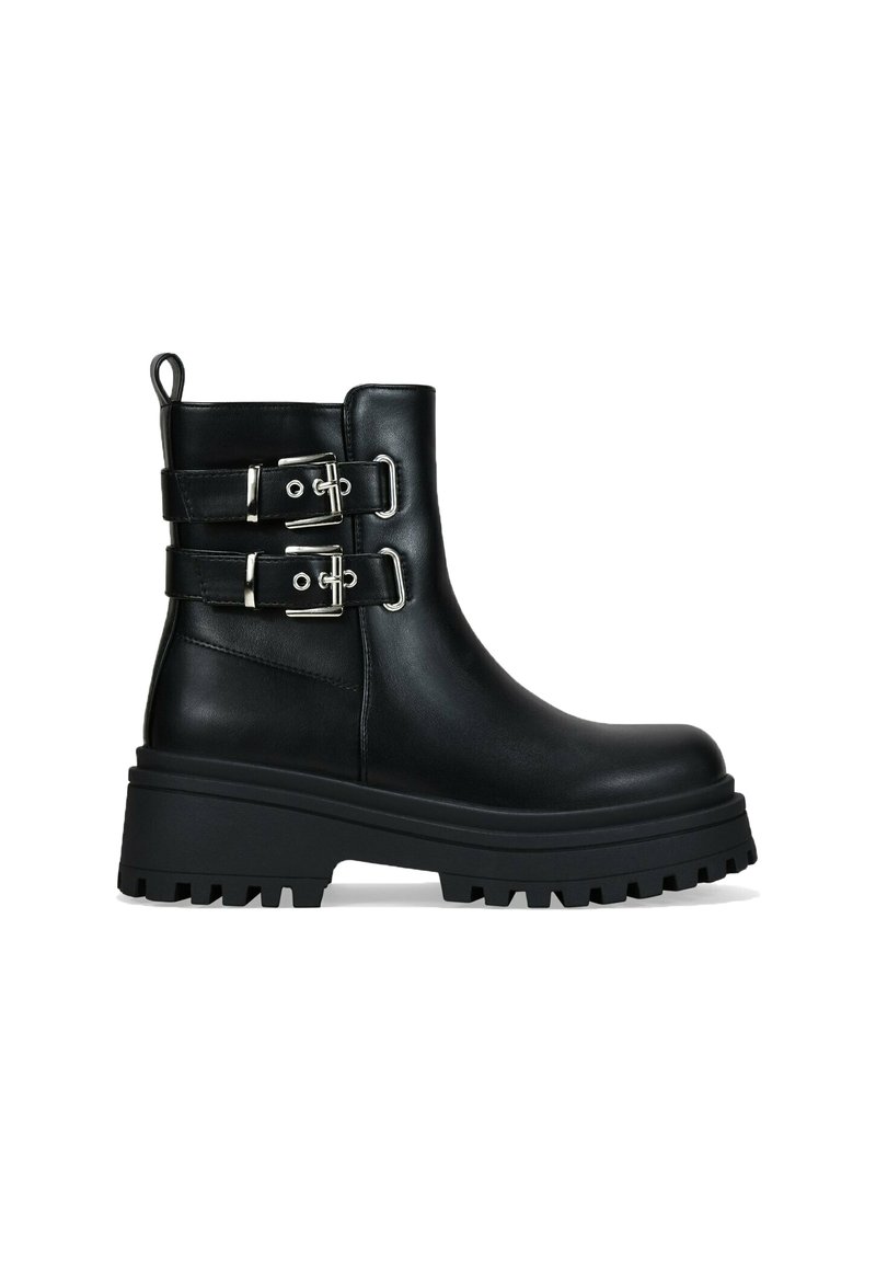 Bota de tobillo de cuero negro con suela gruesa y dentada, dos correas con hebillas plateadas y tira de sujeción en la parte posterior, vista de lado.