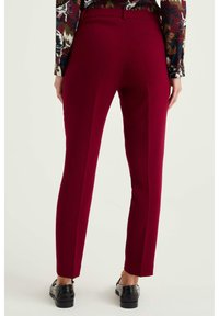 Röda skräddarsydda byxor med slim fit, med en mjuk textur, bälteshällor och en sömdetalj på sidan. I kombination med svarta skor.