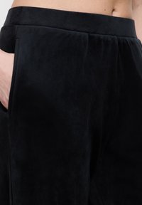 Zwarte suède broek met een soepele textuur, elastische tailleband en zijzakken. De stof heeft een subtiele glans.