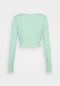 Haut court côtelé à manches longues de couleur vert menthe avec un col large, vu de dos sur un fond blanc.