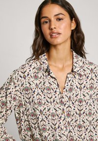 Camicia a maniche lunghe con bottoni in tessuto leggero, caratterizzata da un motivo floreale con accenti multicolori su uno sfondo crema.