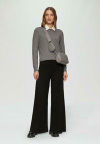 Grijze gebreide trui met een witte kraag, gecombineerd met een wijde zwarte broek en glanzende zwarte schoenen. Grijze schoudertas met een ronde ontwerp.