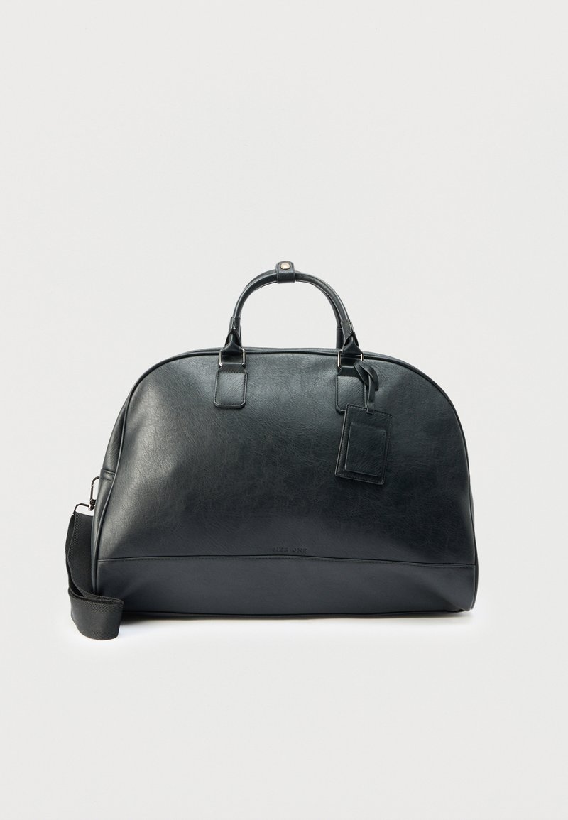 Sac de voyage en cuir noir avec une forme arrondie, double poignées, bandoulière amovible et une étiquette en cuir pour personnalisation.