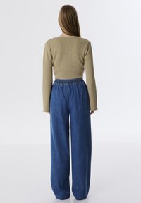 Gebreide, khaki cropped trui met lange mouwen, gecombineerd met losse spijkerbroek met wijde pijpen in blauw, voorzien van een elastische tailleband en een comfortabele pasvorm.