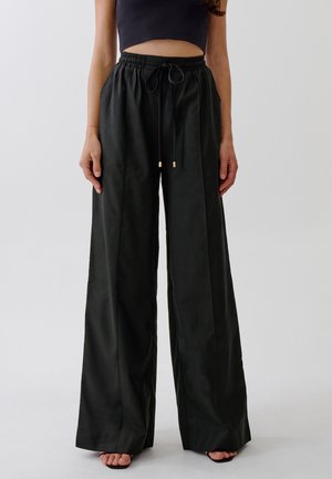 Zwarte, wijde broek met een hoge elastische tailleband, trekkoordsluiting en gouden hardware-accenten. Gladde, lichte stof met een strakke afwerking.