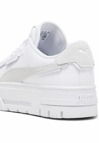 Zapatillas blancas con una franja de gamuza texturada, cuello acolchado y suela de goma gruesa. Presentan un marcado mínimo y un lazo en el talón.