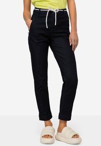 Pantaloni in denim scuro con vita regolabile e accenti bianchi, abbinati a sandali scivolati imbottiti color avorio. Texture liscia, vestibilità affusolata.