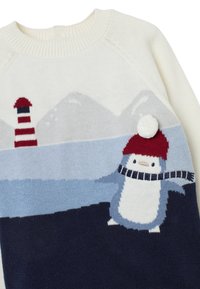 Gebreide trui met een crèmekleurige basis, een blauw en marineblauw ontwerp, een pinguïn met een rode hoed en sjaal, en een vuurtoren op de achtergrond.