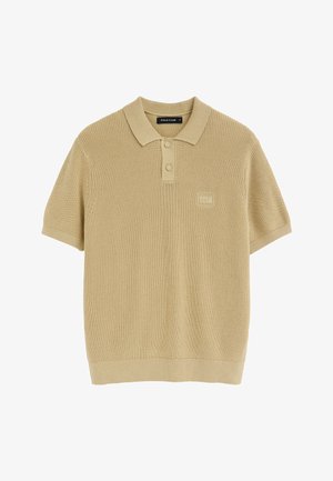 Polo de punto beige de manga corta con cuello, dos botones y un parche con el logo "Polo Club" en el pecho izquierdo.