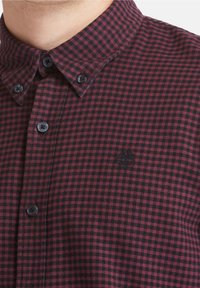 Camicia button-up a quadri rossi e neri con colletto, dotata di bottoni neri e di un logo ricamato discreto sulla parte sinistra del petto.