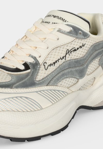 Λευκό και ασημί sneaker Emporio Armani με διχτυωτά πάνελ, χαρακτηριστικό λογότυπο στο πλάι, παχιά υφή στην σόλα και κορδόνια σε εκρού χρώμα.