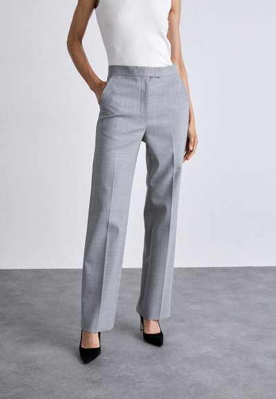 Pantalones gris a medida con un sutil patrón de cuadros, diseño de pierna recta y sin bolsillos visibles, combinados con zapatos de tacón alto negros.