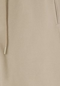 Beige textured fabric with a drawstring and a pocket seam, highlighting material and garment details close-up.