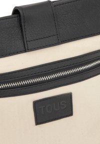 Czarna i beżowa torba na ramię z teksturowanym materiałowym korpusem, skórzanymi detalami, srebrnym suwakiem oraz czarną naszywką z logo wygrawerowanym "TOUS".