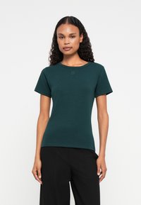 Tricou verde, potrivit, cu mâneci scurte și decolteu tăiat. prezintă branding subtil "HUGO" pe față. Textură netedă.