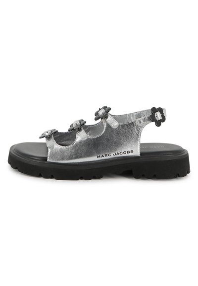 Ασημί μεταλλικά σανδάλια με τρία μαύρα λουλουδένια διακοσμητικά, ρυθμιζόμενο λουράκι στη φτέρνα και χοντρή μαύρη σόλα από καουτσούκ. Λογότυπο της μάρκας στη πλευρά.