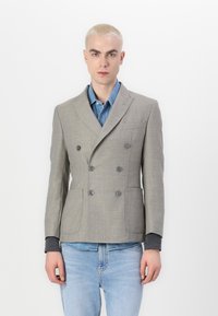 Hallgray kahekordne ülikond, millel on tekstuurne viimistlus, klapiga krae ja kaks eesmist taskut, kantuna denimpuseriga.
