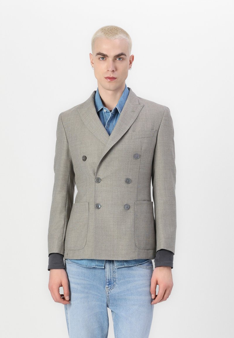 Hallgray kahekordne ülikond, millel on tekstuurne viimistlus, klapiga krae ja kaks eesmist taskut, kantuna denimpuseriga.