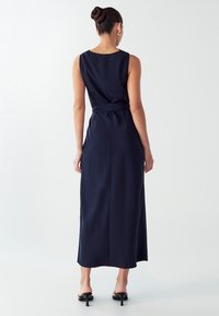 Morska plava maksi haljina bez rukava s uskim korzetom i pojasom u struku. Glatka, mat tkanina s ravnim krojem i minimalnim detaljima šavova.