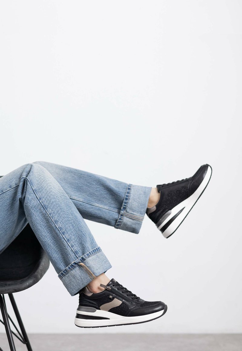 Zapatillas negras con paneles texturizados y suela gruesa blanca. Llevadas con unos pantalones vaqueros de mezclilla cortos de color azul claro con dobladillos deshilachados.