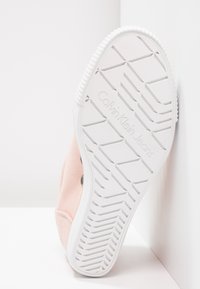 Růžová teniska s bílou gumovou podrážkou s texturovaným vzorem, zdobená nápisem "Calvin Klein Jeans" na spodní straně, vyrobená z měkkého materiálu.