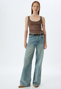 Bruine geribbelde tanktop, hooggewaagde vervaagde blauwe wijde jeans met een zwarte riem en beige hakken. Soepele textuur en casual pasvorm.